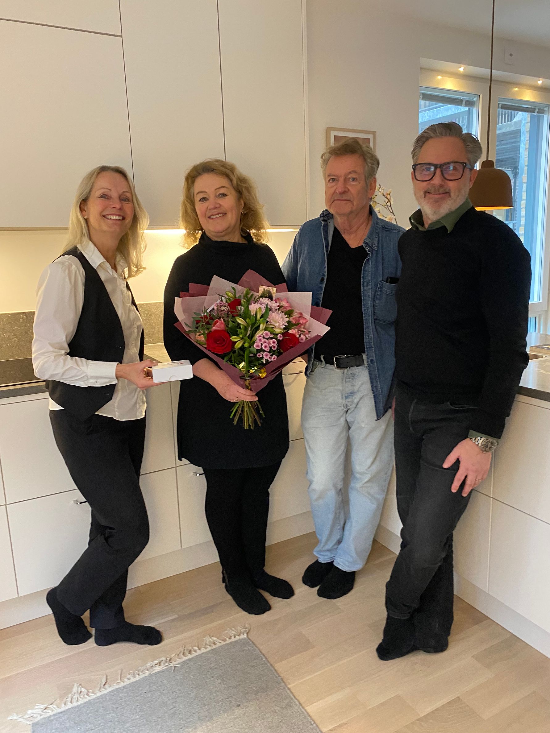 Fyra personer står i ett kök, varav en kvinna håller en blomsterbukett