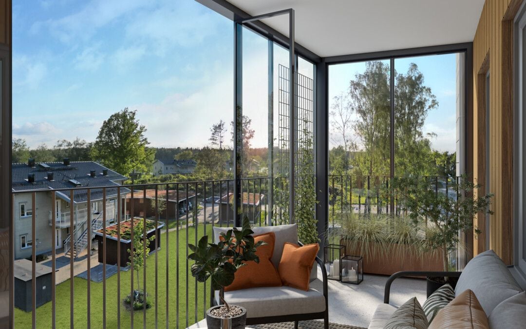 Inglasad balkong med utsikt över grönska, moderna byggnader och en välskött trädgård, möblerad med soffor, kuddar och krukväxter