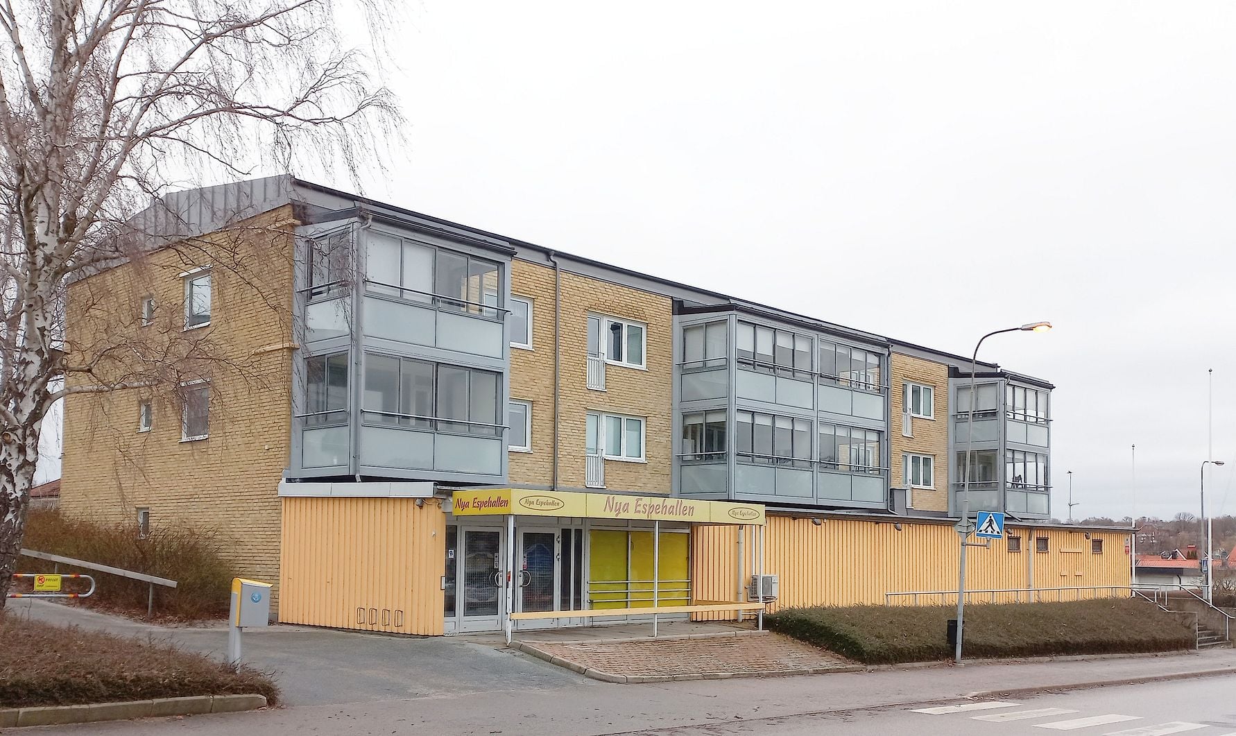 Lägenhetsbyggnad i tegel med glasbalkonger, belägen vid en gata med trottoar och övergångsställe