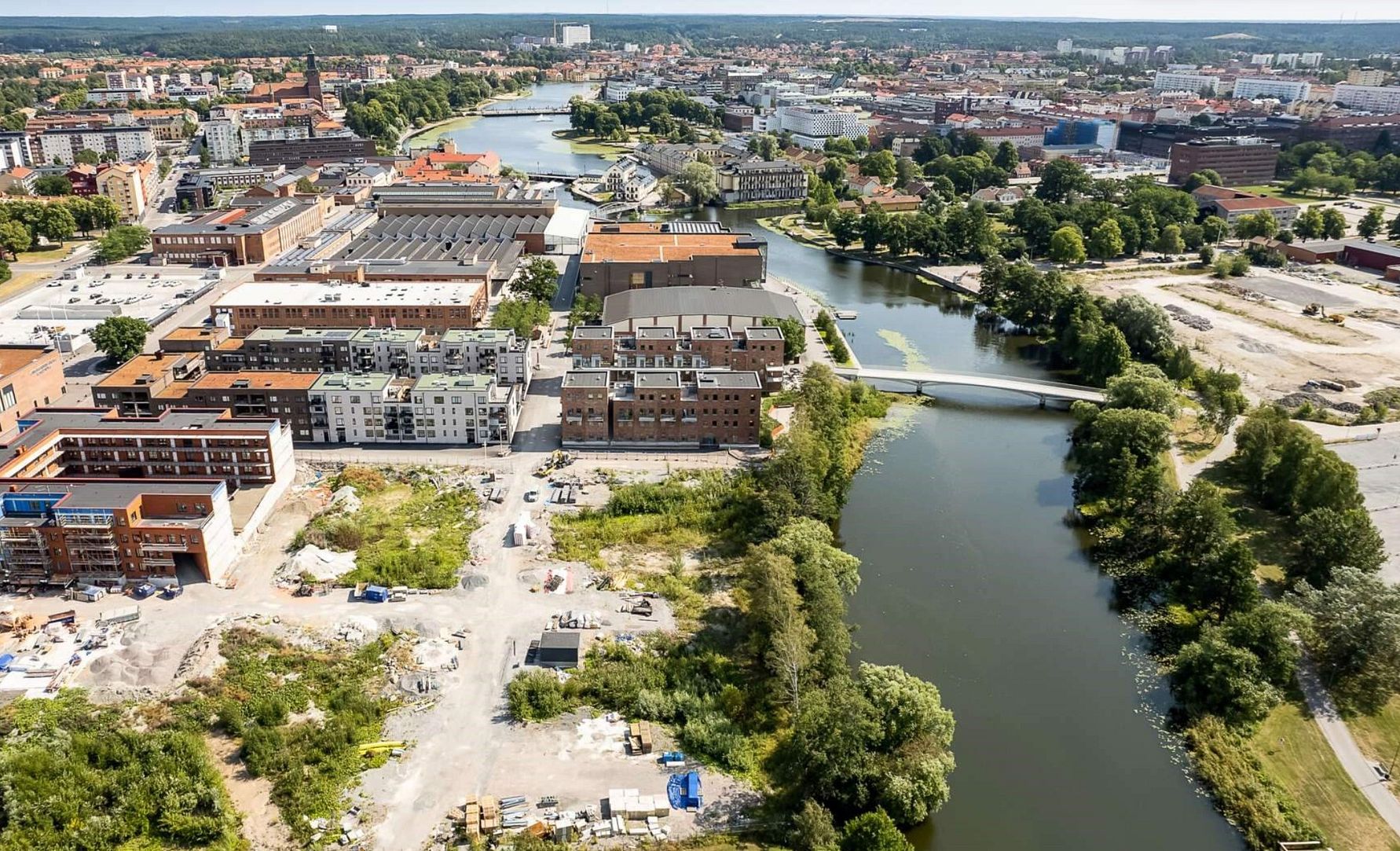 Flygbild över en stad med en flod som slingrar sig genom området, omgiven av byggnader, parker och öppna ytor
