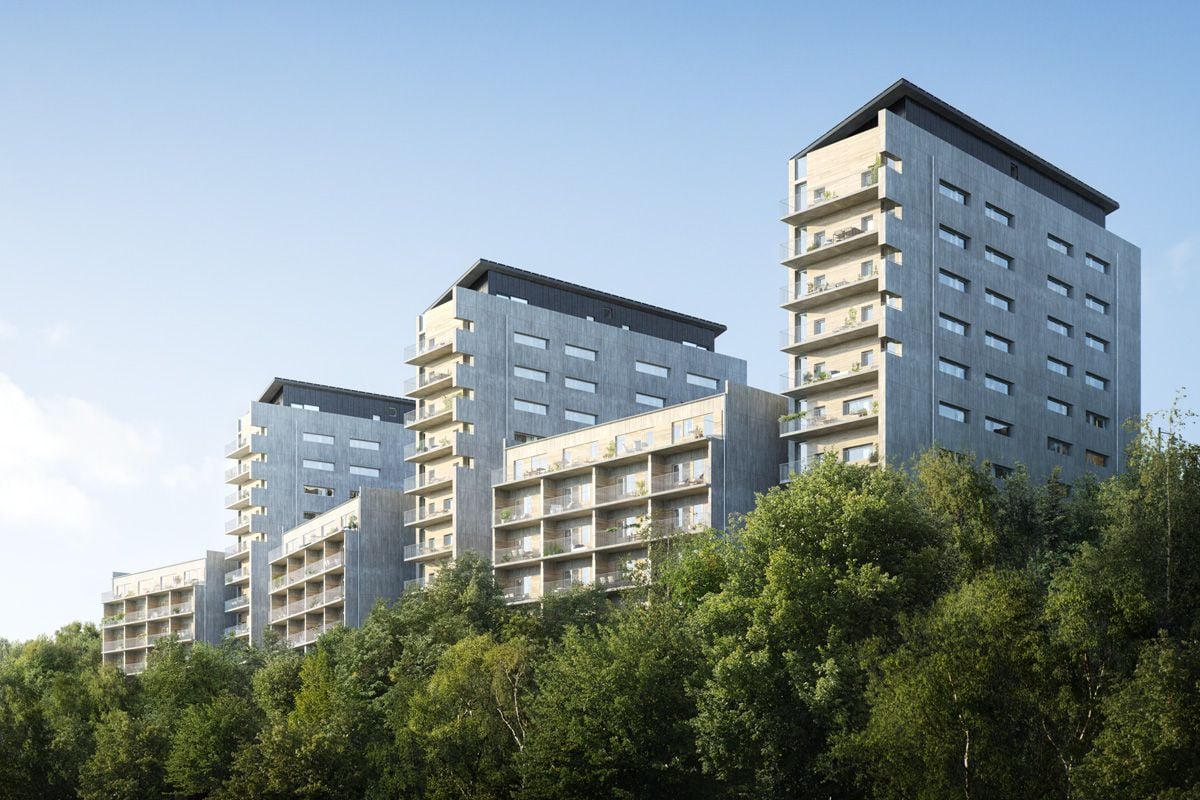 Tre moderna flerbostadshus med grå fasader och stora fönster, omgivna av gröna träd under en klarblå himmel