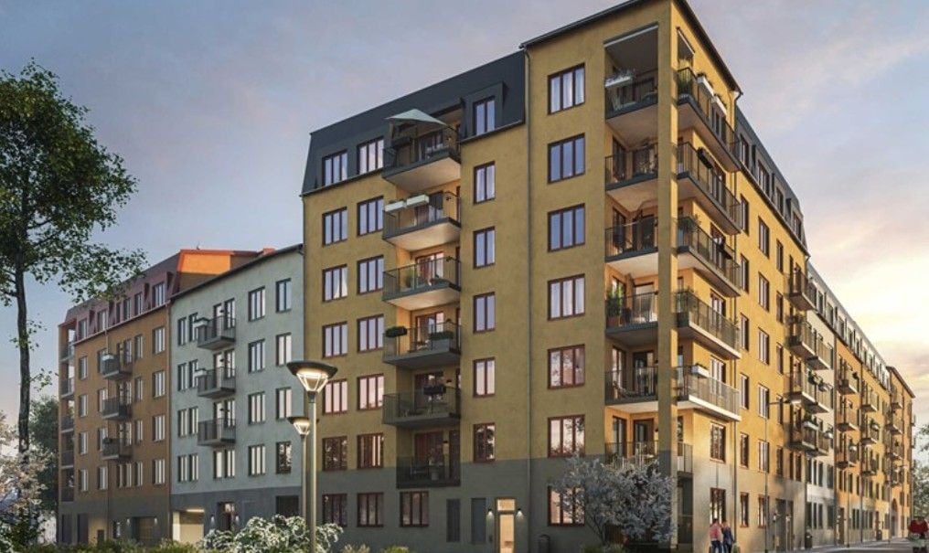 Flerbostadshus med gul och grå fasad, flera balkonger och omgivande träd i ett stadsområde under solnedgång