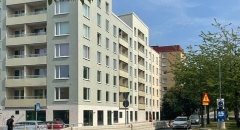 Modern flerfamiljshus med ljusa fasader, balkonger och parkeringsplatser i förgrunden. Träd och en blå himmel i bakgrunden