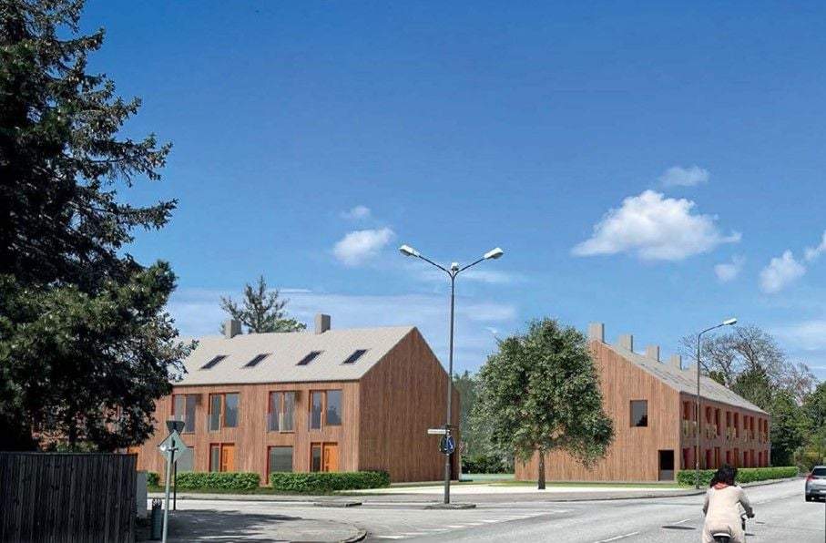 Två moderna flerfamiljshus med träfasader vid en vägkorsning under en klar blå himmel. En person på cykel syns i förgrunden