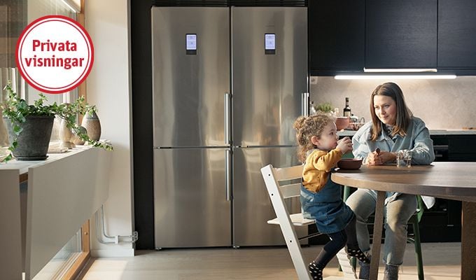 Kök med modern inredning, ett stort kylskåp i rostfritt stål, och ett runt bord där två personer sitter