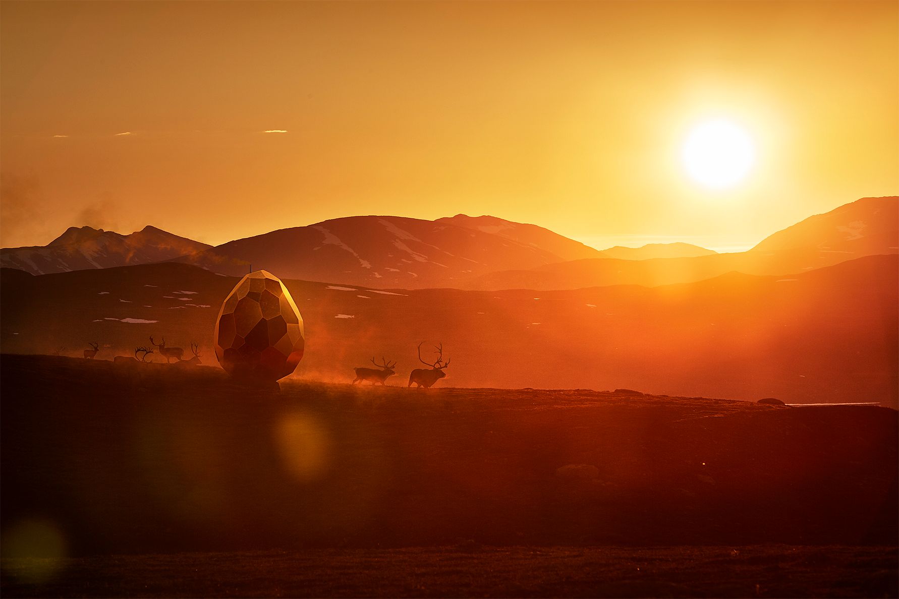 Solnedgång över ett bergslandskap med ett stort, gyllene äggformigt objekt och hjortar på en gräsklädd kulle