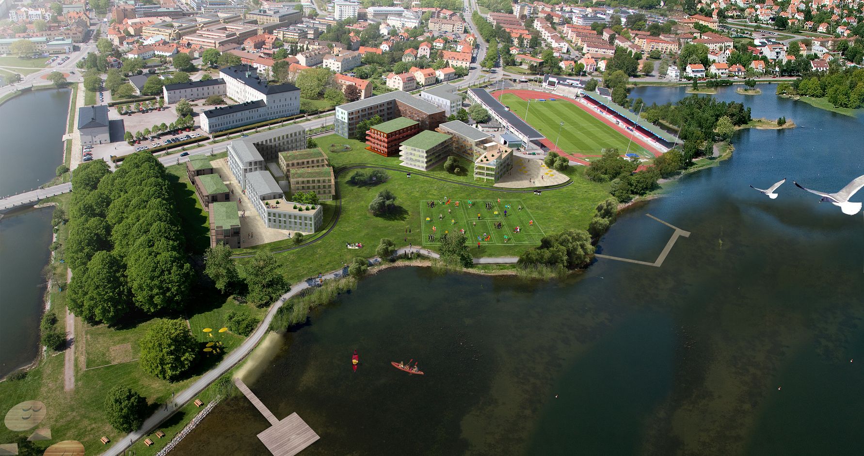 Flygvy över ett stadsområde med byggnader, parker, en idrottsarena och vatten med bryggor och små båtar
