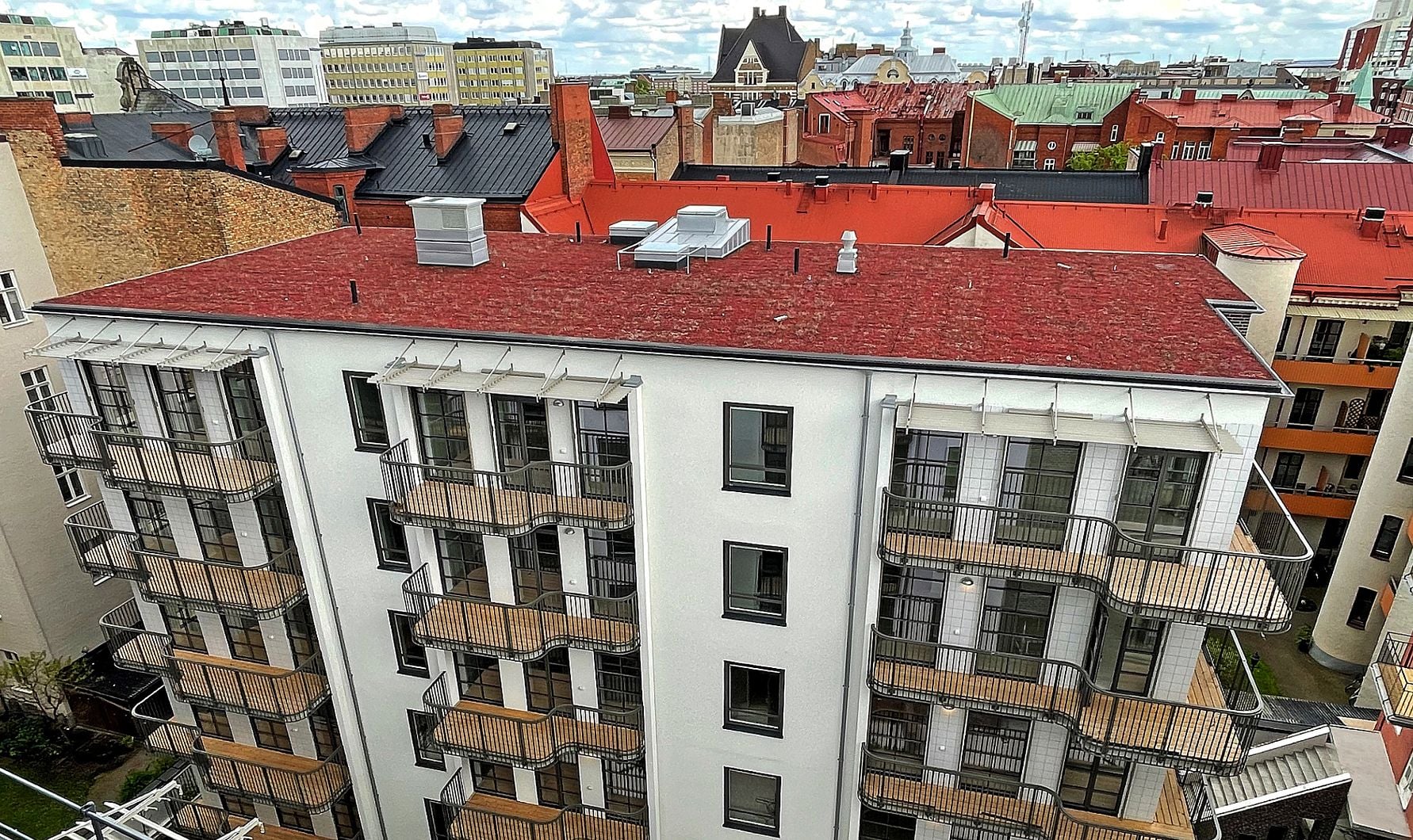 Flerbostadshus med vit fasad och röda tak, omgiven av andra byggnader i stadsmiljö