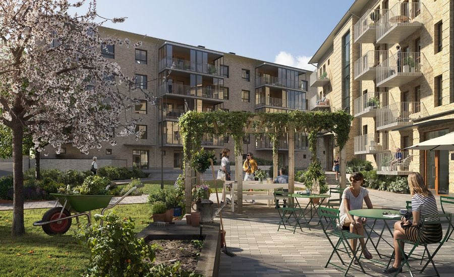 Flerbostadshus i sten med balkonger, grönskande innergård med pergola, trädgårdsmöbler och människor i en social miljö