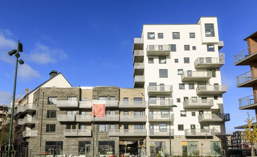 Modern flerfamiljshus med fasader av tegel och ljus puts, omgivet av byggnadsställningar och en klar blå himmel