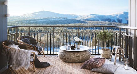 Balkong med utsikt över snöklädda berg och skog, möblerad med fåtöljer, bord och kuddar