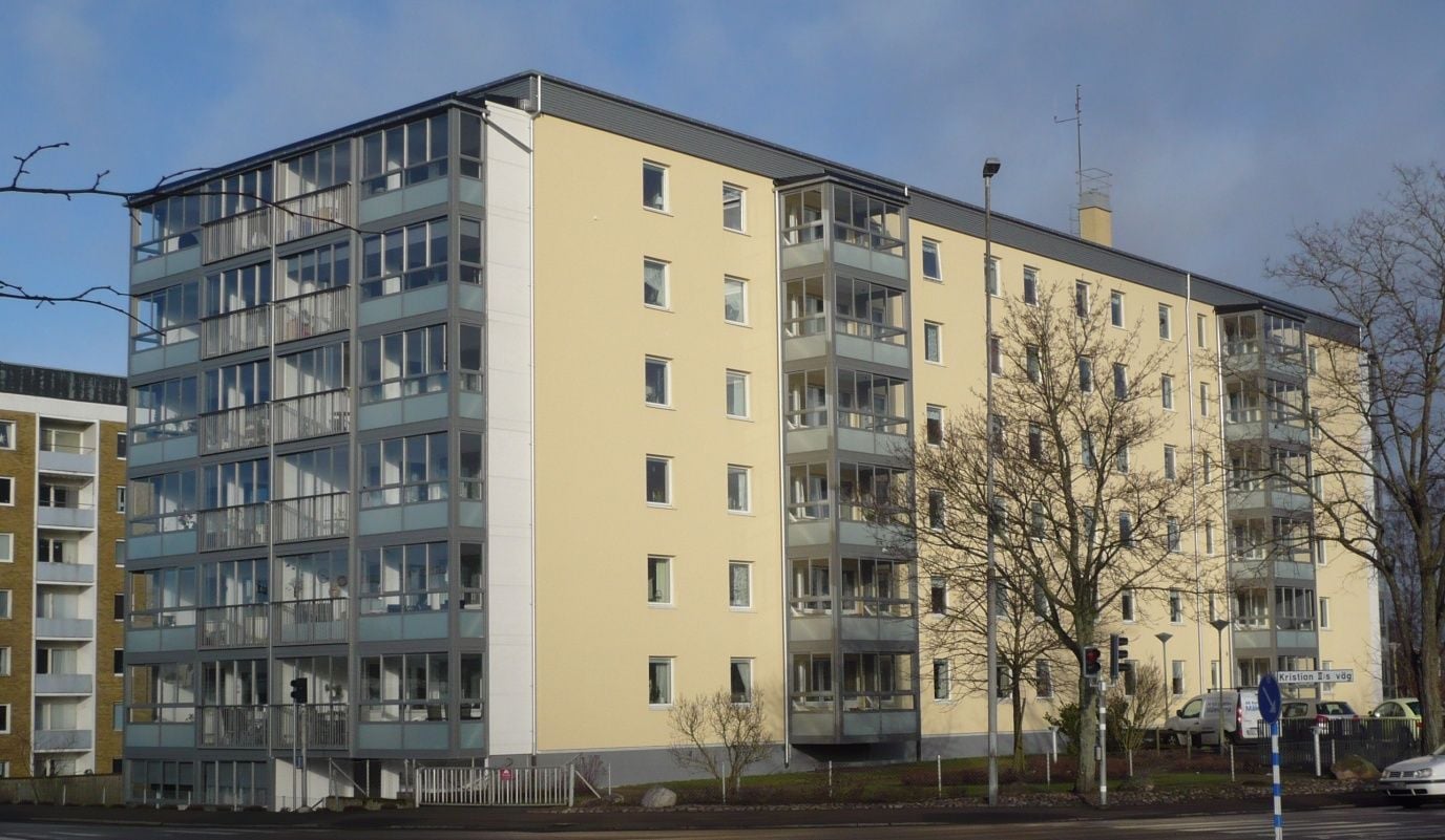 Flerfamiljshus med ljusgul fasad och balkonger, beläget vid en gata med träd och gatlampor
