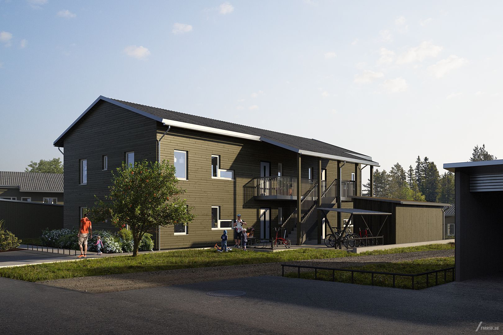 Tvåvåningshus med träfasad i mörkgrön färg, omgiven av grönska och en asfalterad väg i ett bostadsområde. Cyklister och människor syns vid byggnaden