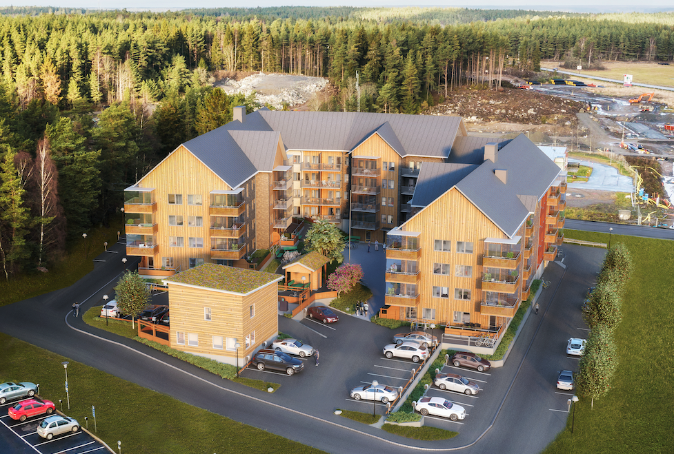 Bostadsområde med träbyggnader omgivna av parkeringsplatser, grönområden och skog i bakgrunden