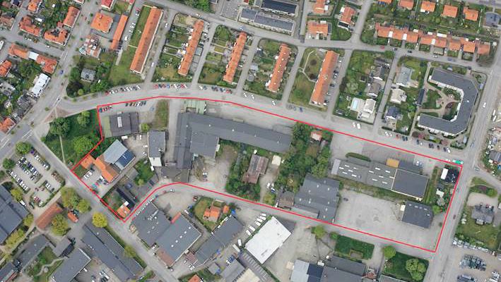 Flygfoto över ett område med byggnader, vägar och bostadshus, där en röd linje markerar en specifik fastighet