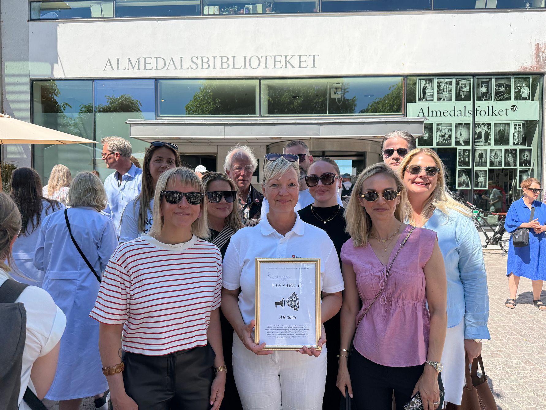 Grupp av personer utanför Almedalsbiblioteket, en person håller upp ett inramat diplom