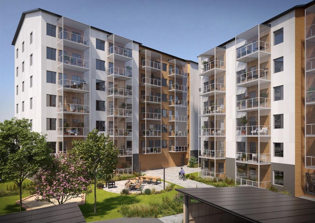 Flera moderna flerbostadshus med vita och bruna fasader, balkonger och en grön innergård med träd och sittplatser under klarblå himmel