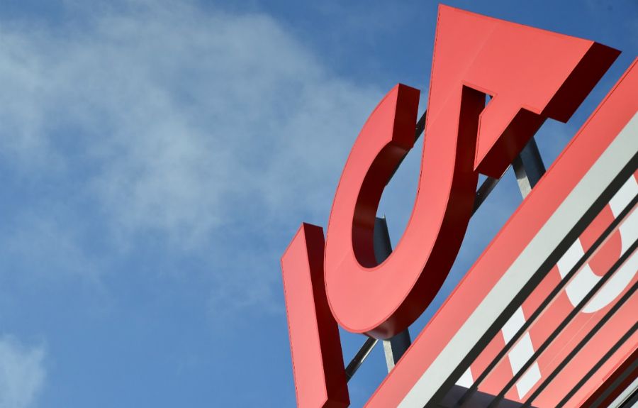Röd ICA-skylt på ett hustak mot en blå himmel med moln
