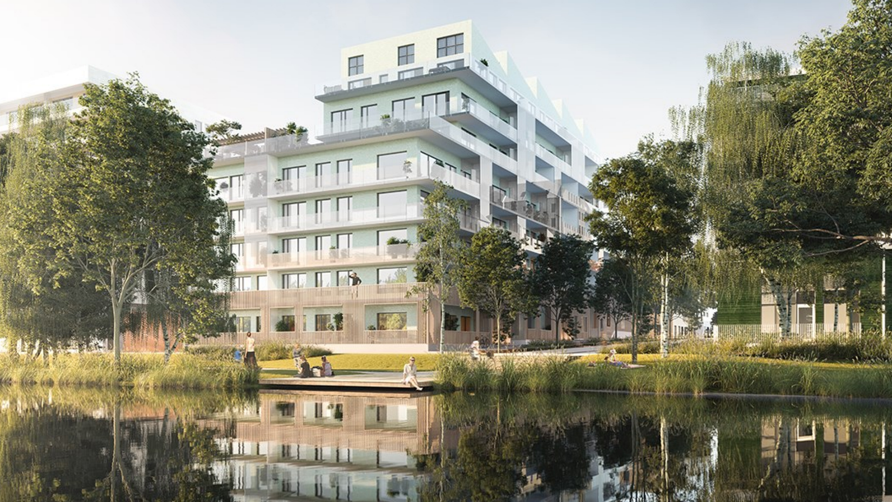 Modernt flerfamiljshus med glasfasad vid en sjö, omgiven av träd och grönska