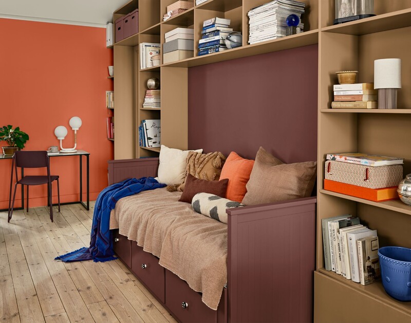 Rum med inbyggd bokhylla och dagbädd, färgglada kuddar i orange och bruna toner, skrivbord med dekorationer, och väggar i orange och vinrött