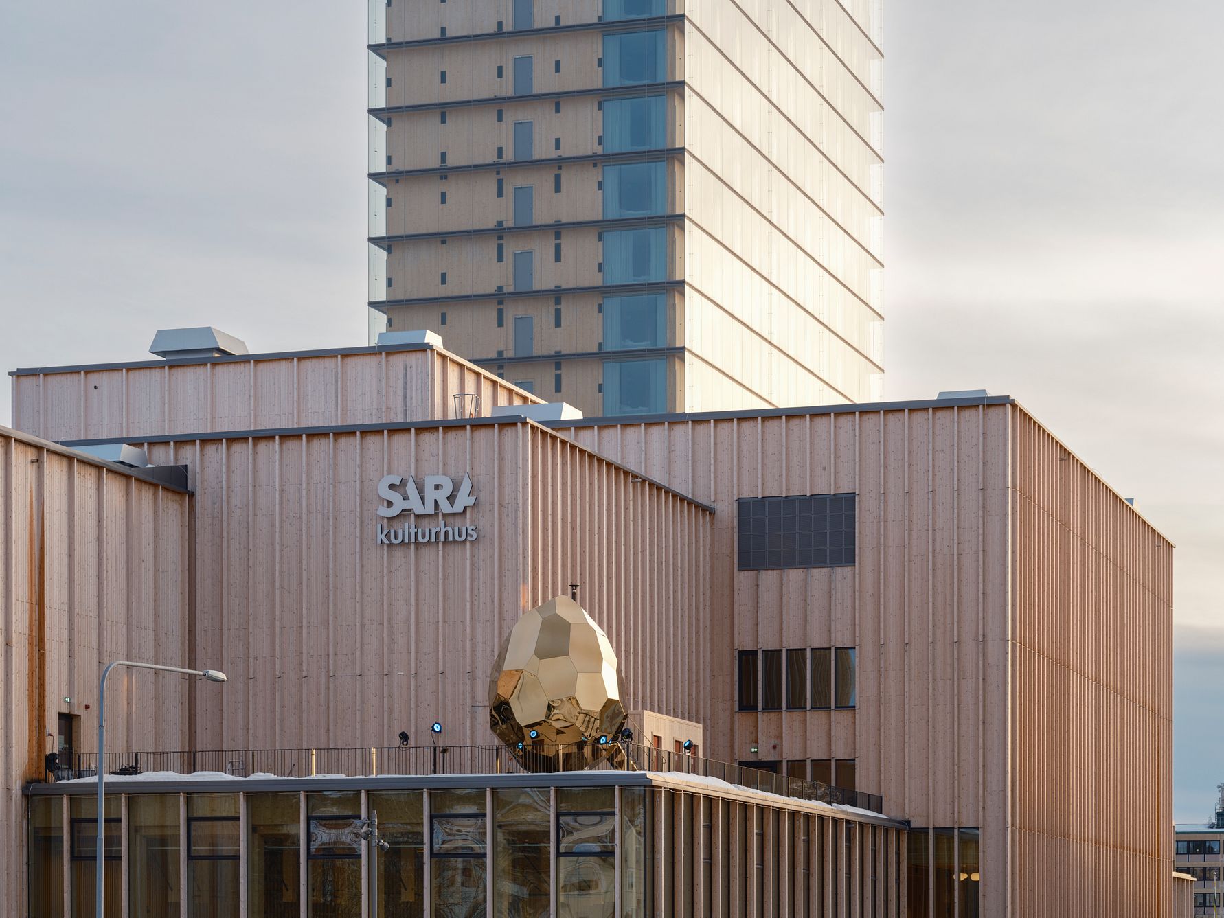 Sara kulturhus med en modern träfasad och ett högt torn i bakgrunden under en ljus himmel