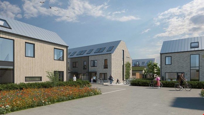 Nybyggda moderna hus med trä- och stenfasader, omgivna av grönska och blommor, med personer som promenerar och cyklar på en bred gångväg under en klar blå himmel