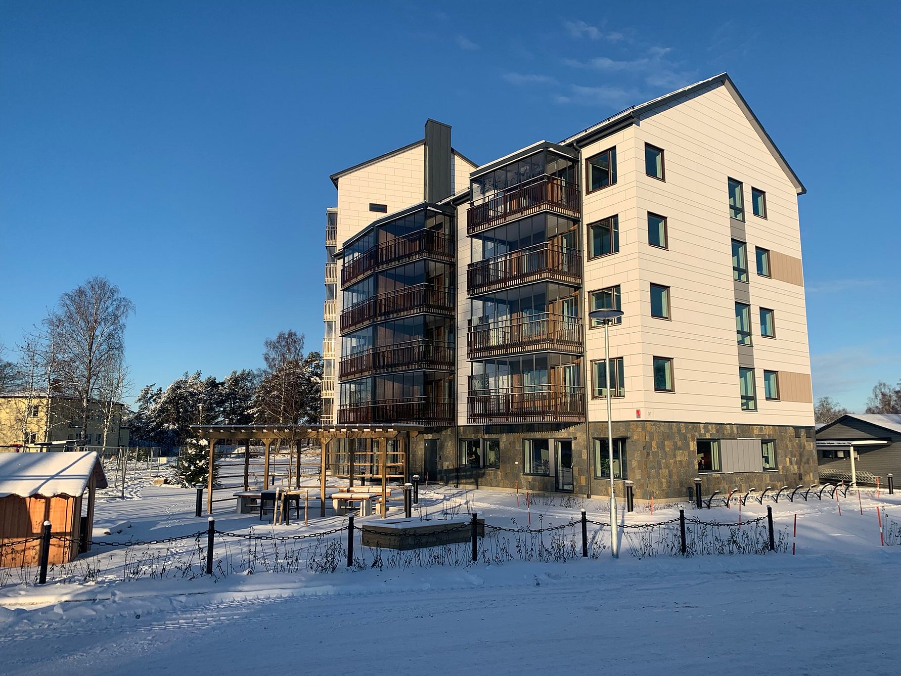 Modern flerfamiljshus med balkonger, omgivna av snö och vinterlandskap under en klar blå himmel