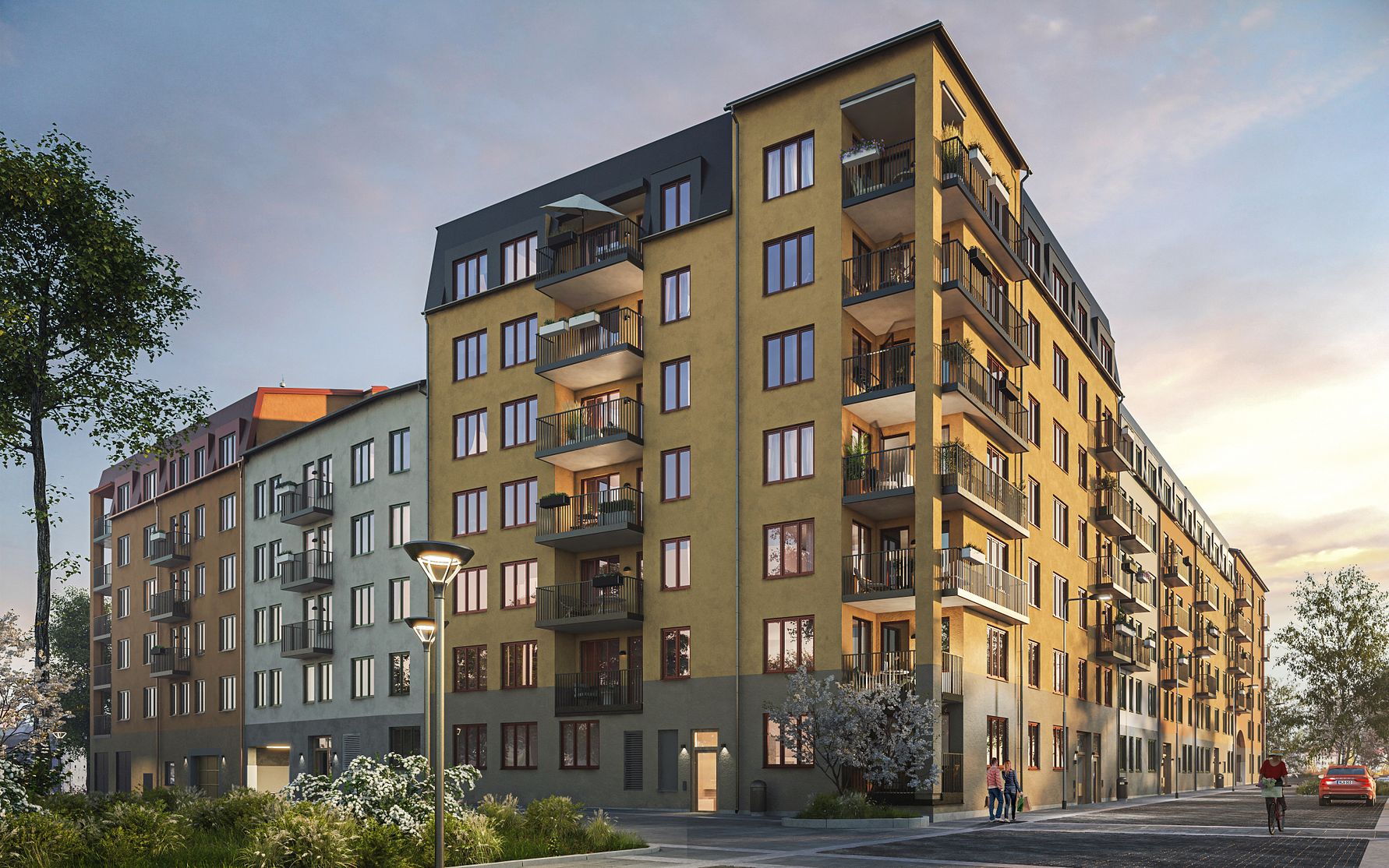 Flerfamiljshus med gul fasad, balkonger och flera våningar, omgivet av grönska och gångväg under solnedgång