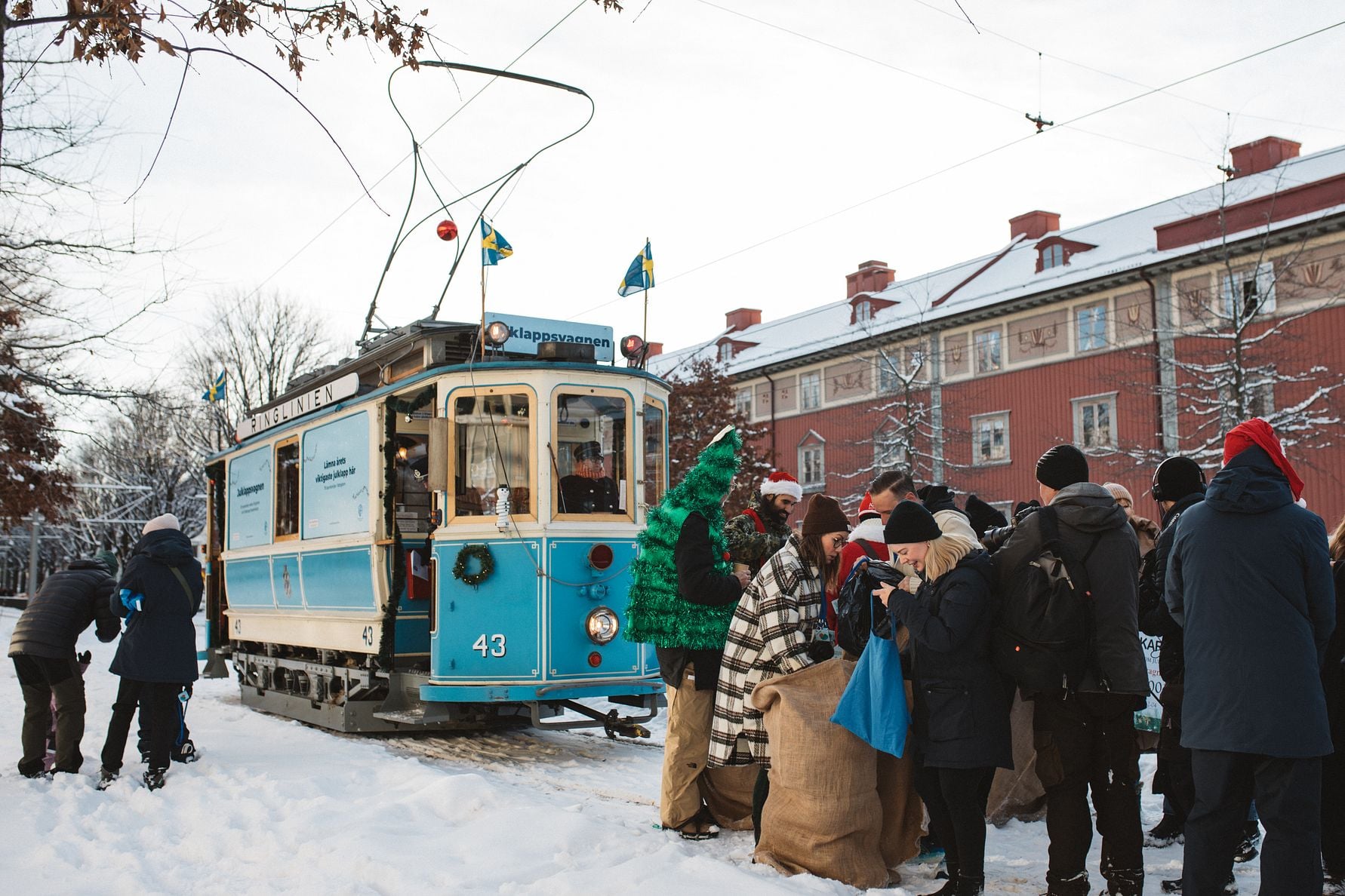 Blå spårvagn vid ett snöklätt område med människor som deltar i en julaktivitet