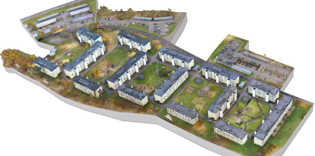 Flygvy av ett bostadsområde med flera flerfamiljshus, grönområden och parkeringsplatser