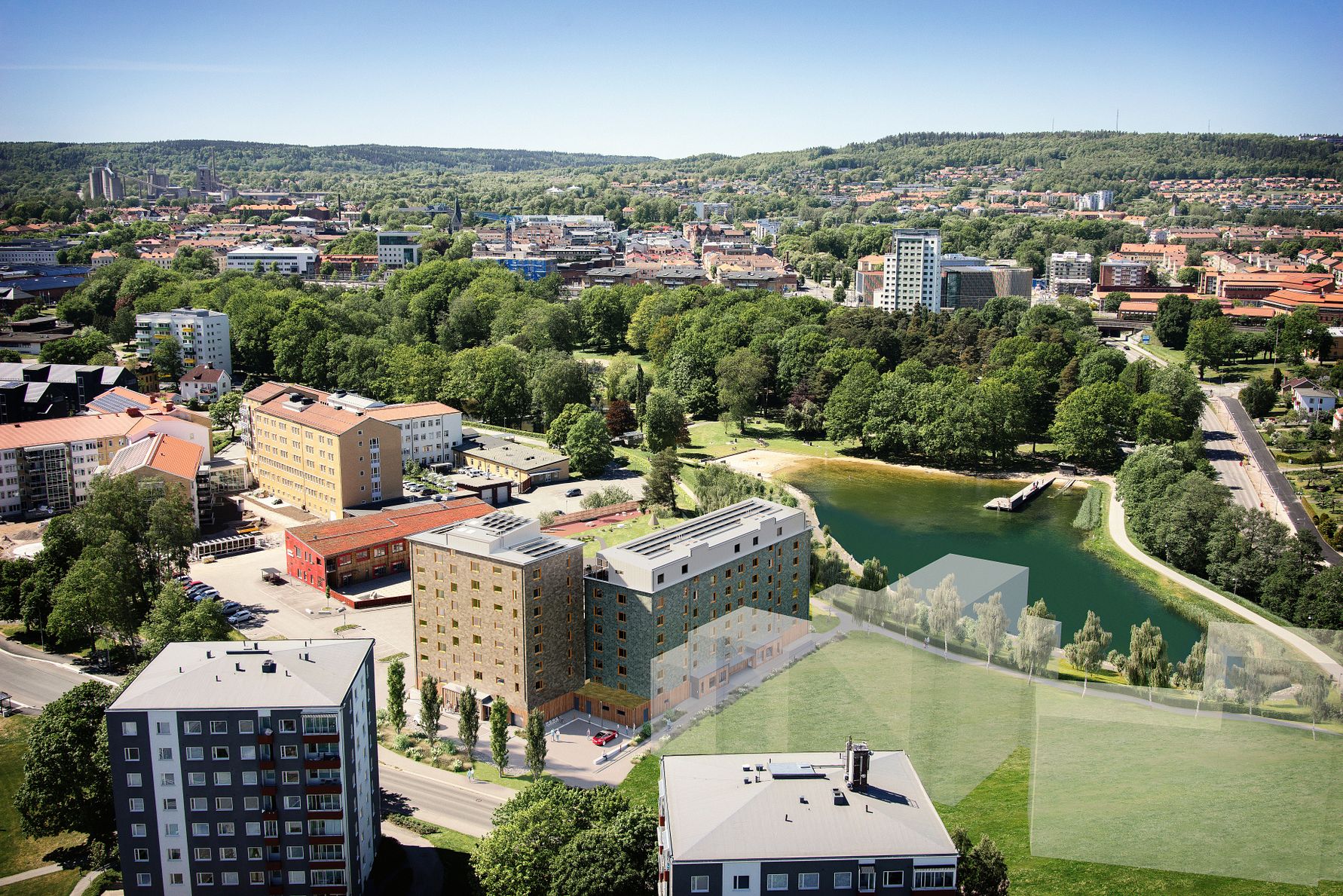 Flygvy över ett bostadsområde med flerfamiljshus, grönområden och en park med en liten sjö, omgiven av stadsmiljö och skog i fjärran