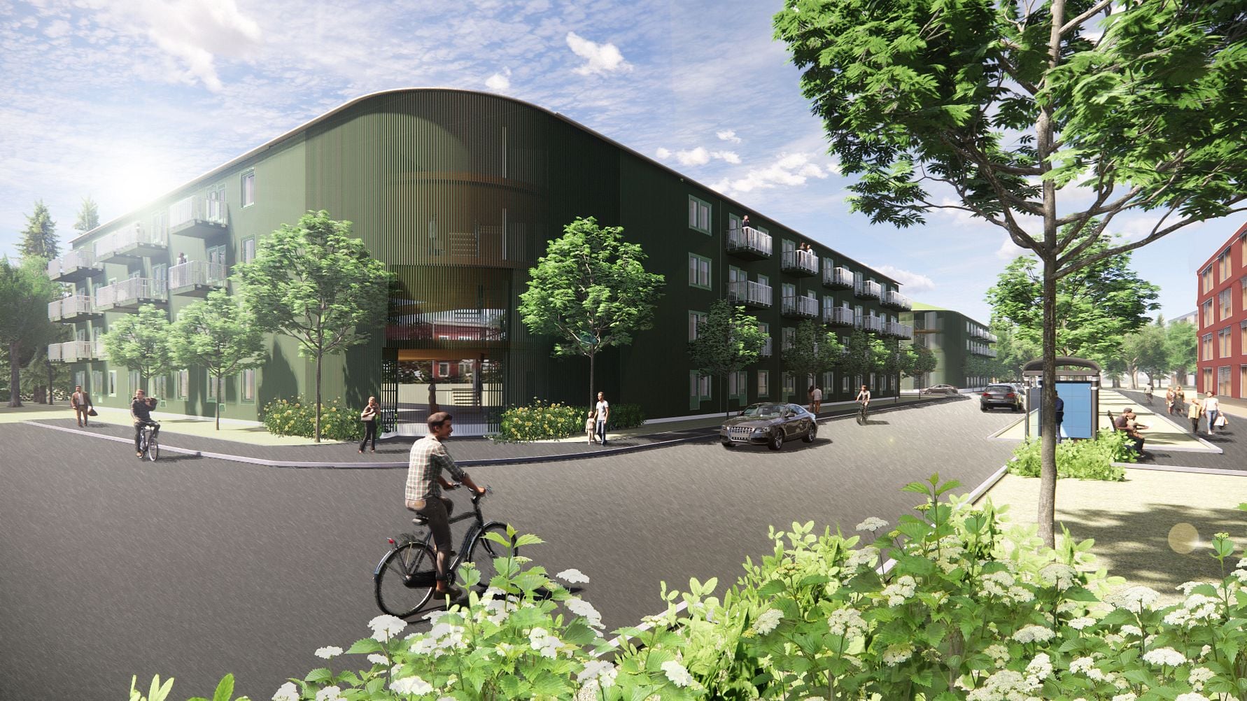 Grön modern byggnad med fyra våningar, omgiven av träd och grönska, med människor som promenerar och cyklar på en solbelyst gata