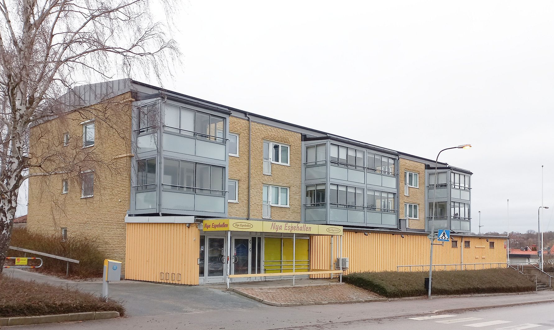 Lägenhetsbyggnad i tegel med glasbalkonger, belägen vid en gata med trottoar och övergångsställe