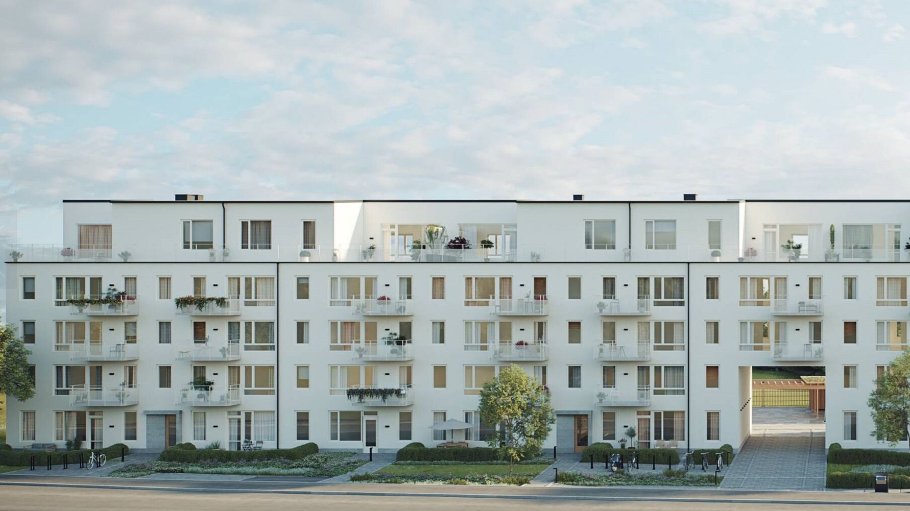 Vit modern flerfamiljsbyggnad med balkonger och grönska framför, under en himmel med lätta moln