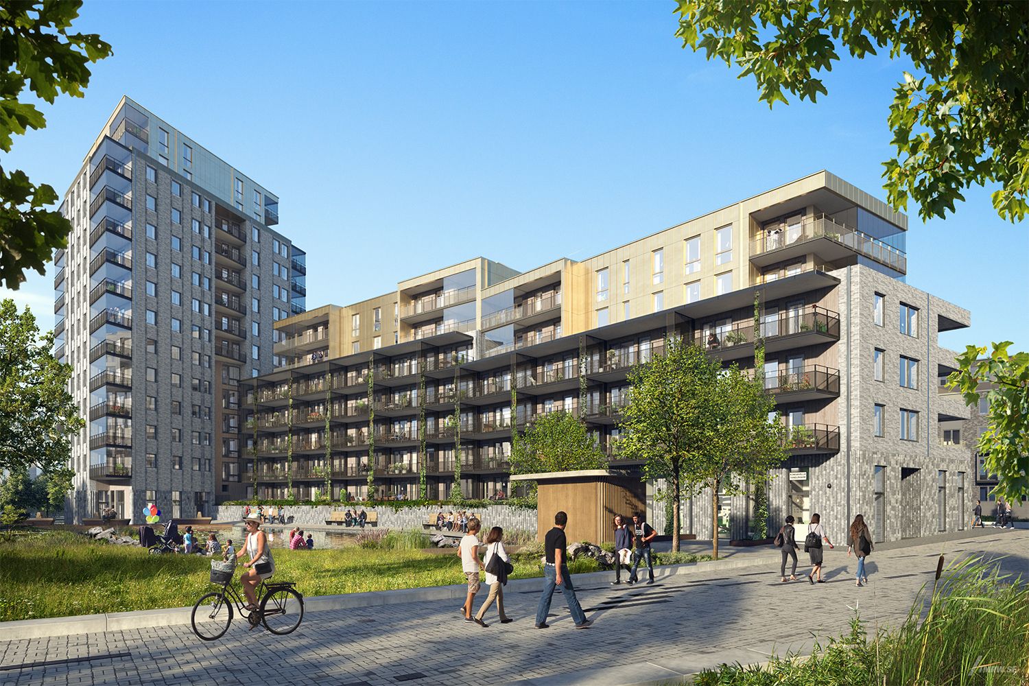 Modern bostadskomplex med flera våningar, omgiven av grönområden och en gångväg där människor promenerar och cyklar. Klarblå himmel i bakgrunden