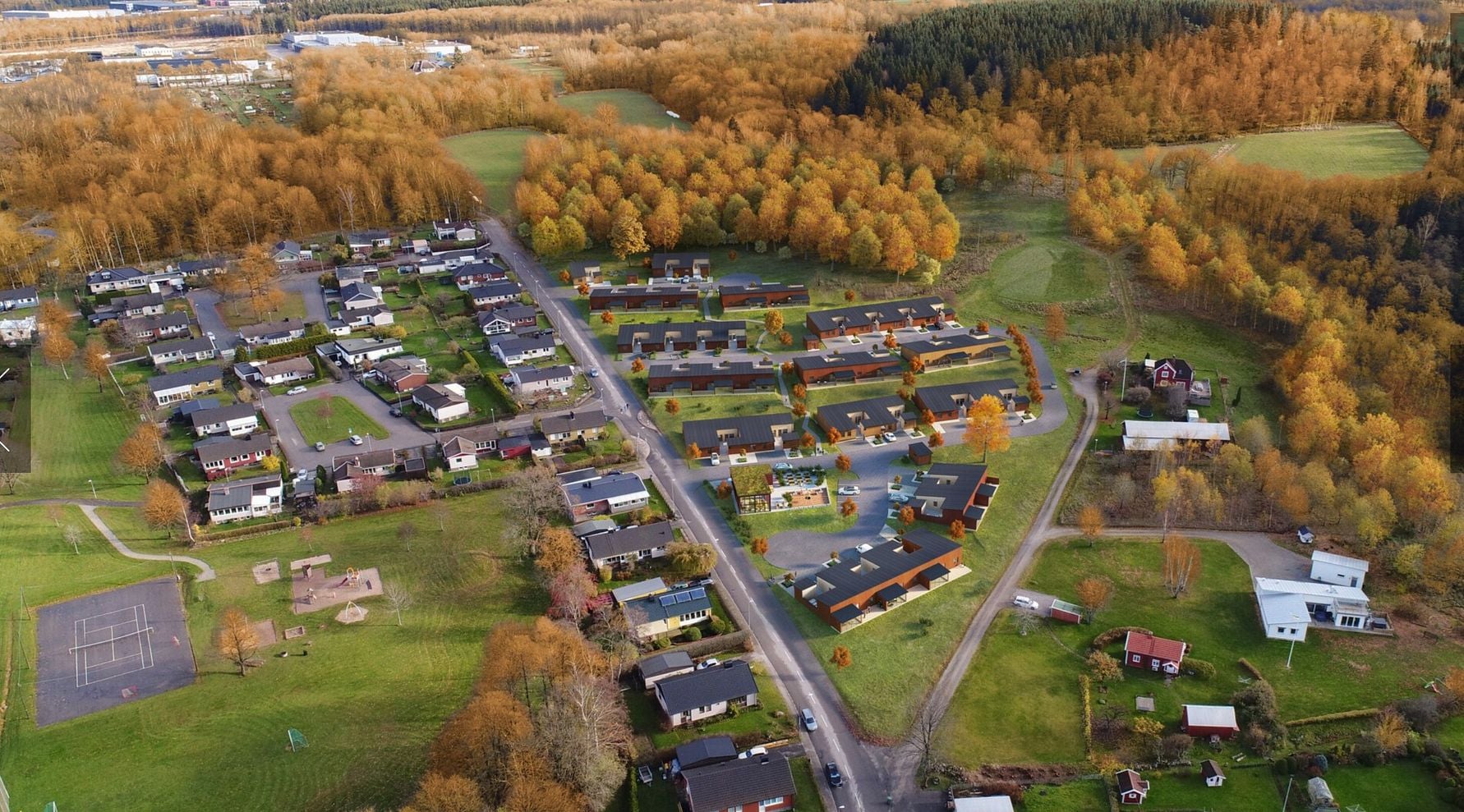 Flygvy över ett bostadsområde med hus, trädgårdar och omgivande skog i höstfärger. Grönområden, lekplatser och en väg synliga
