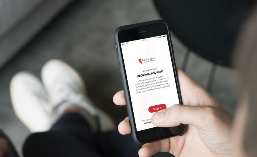 En person håller en smartphone som visar en skärm med text och en röd knapp för inloggning