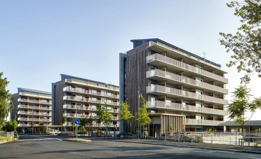 Moderna flerfamiljshus med balkonger, omgivna av träd och gångvägar i ett stadsområde