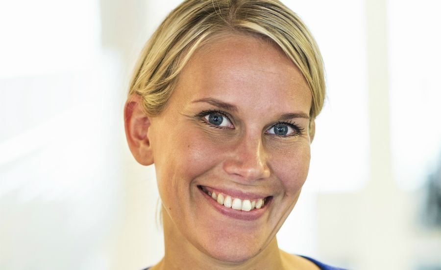 Porträtt av en person med blont hår och blå tröja, med en ljus bakgrund