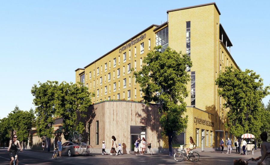 Byggnad i gul tegel med flera våningar, omgiven av träd och människor som rör sig på gatan