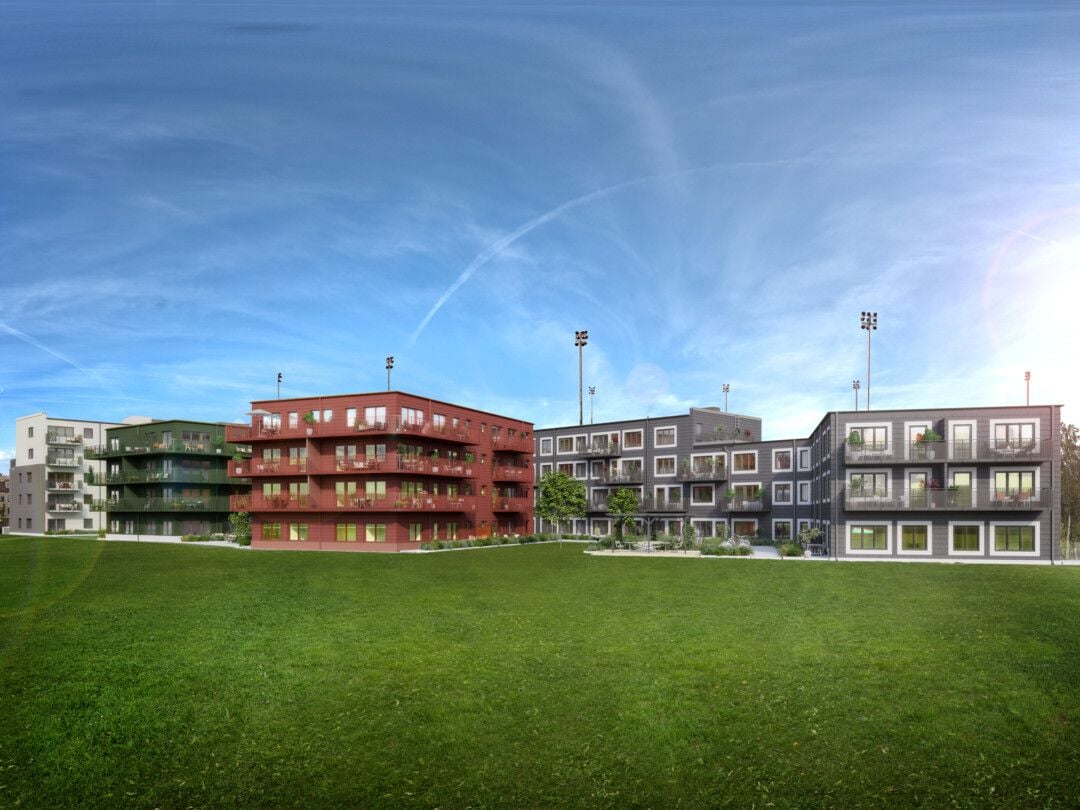 Modern flerfamiljshus med färgade fasader belägna vid en stor gräsplan under klar blå himmel