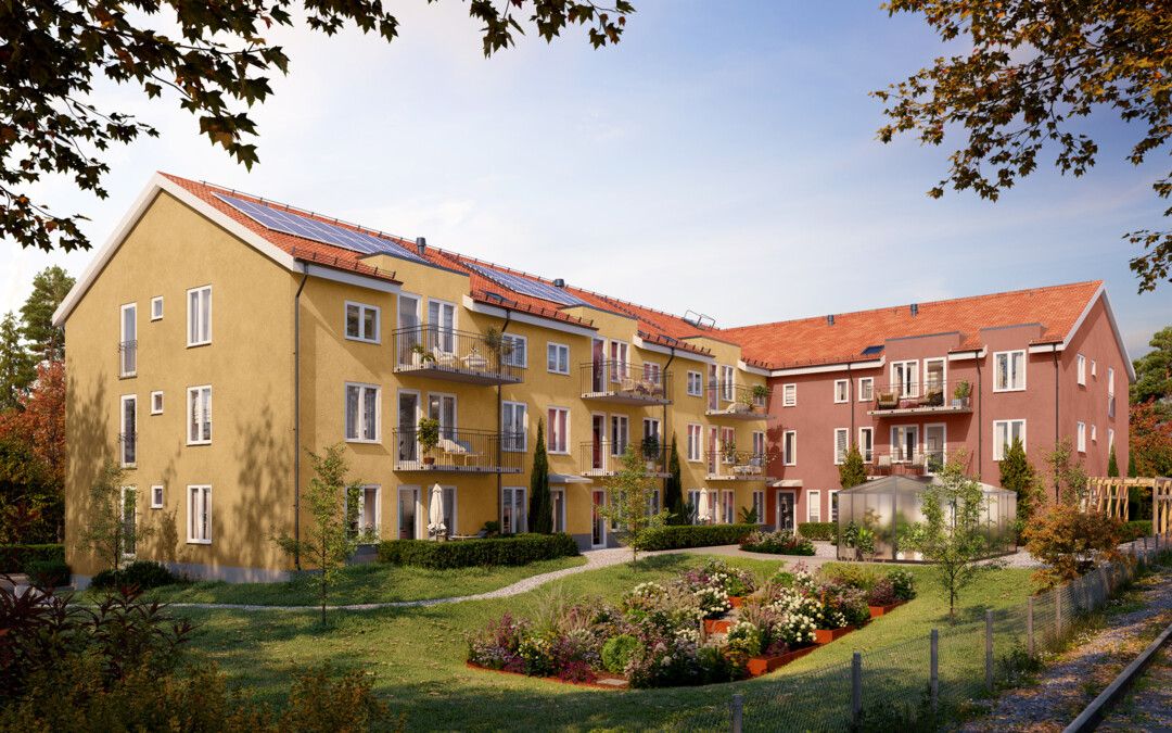 Flerfamiljshus med gul och röd fasad, balkonger och solpaneler på taket, omgivna av en grön trädgård under en klar blå himmel