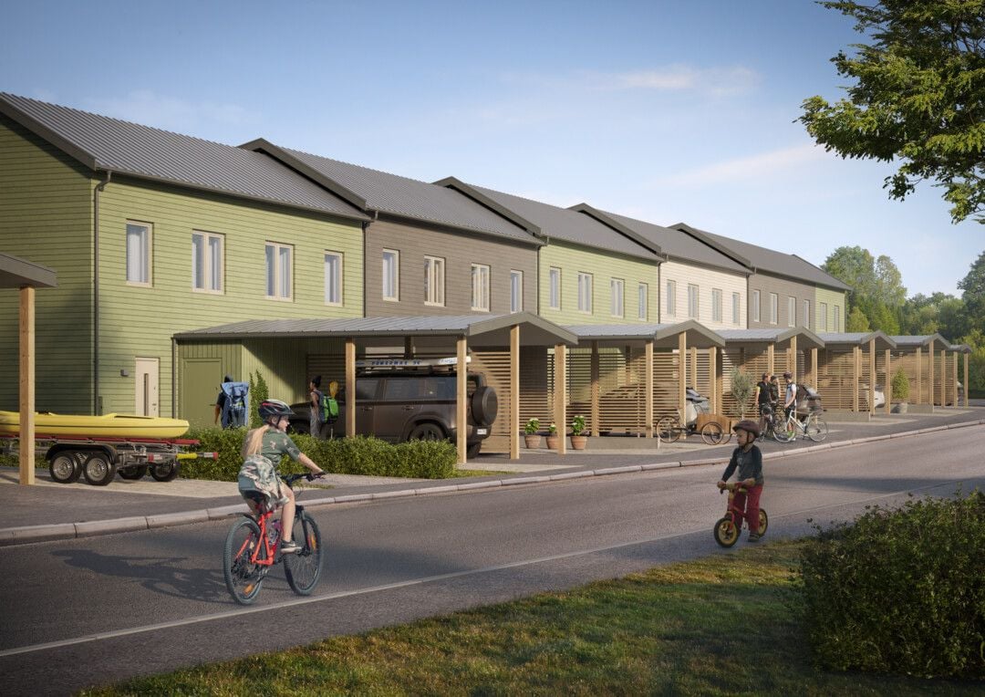 Rad av moderna radhus med gröna och grå fasader, försedda med carportar. Två cyklister ses på gatan framför husen, omgivna av träd och grönska