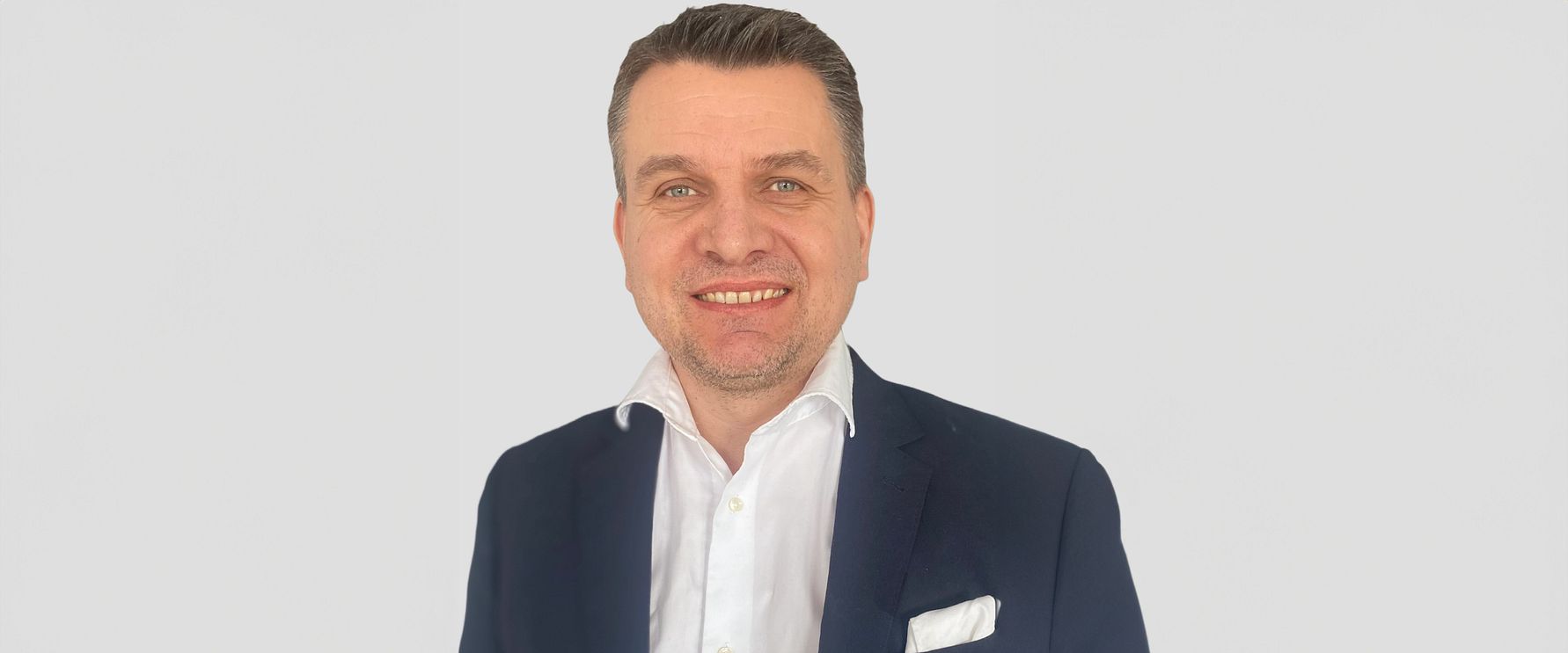 Man i mörkblå kavaj och vit skjorta mot en ljus bakgrund