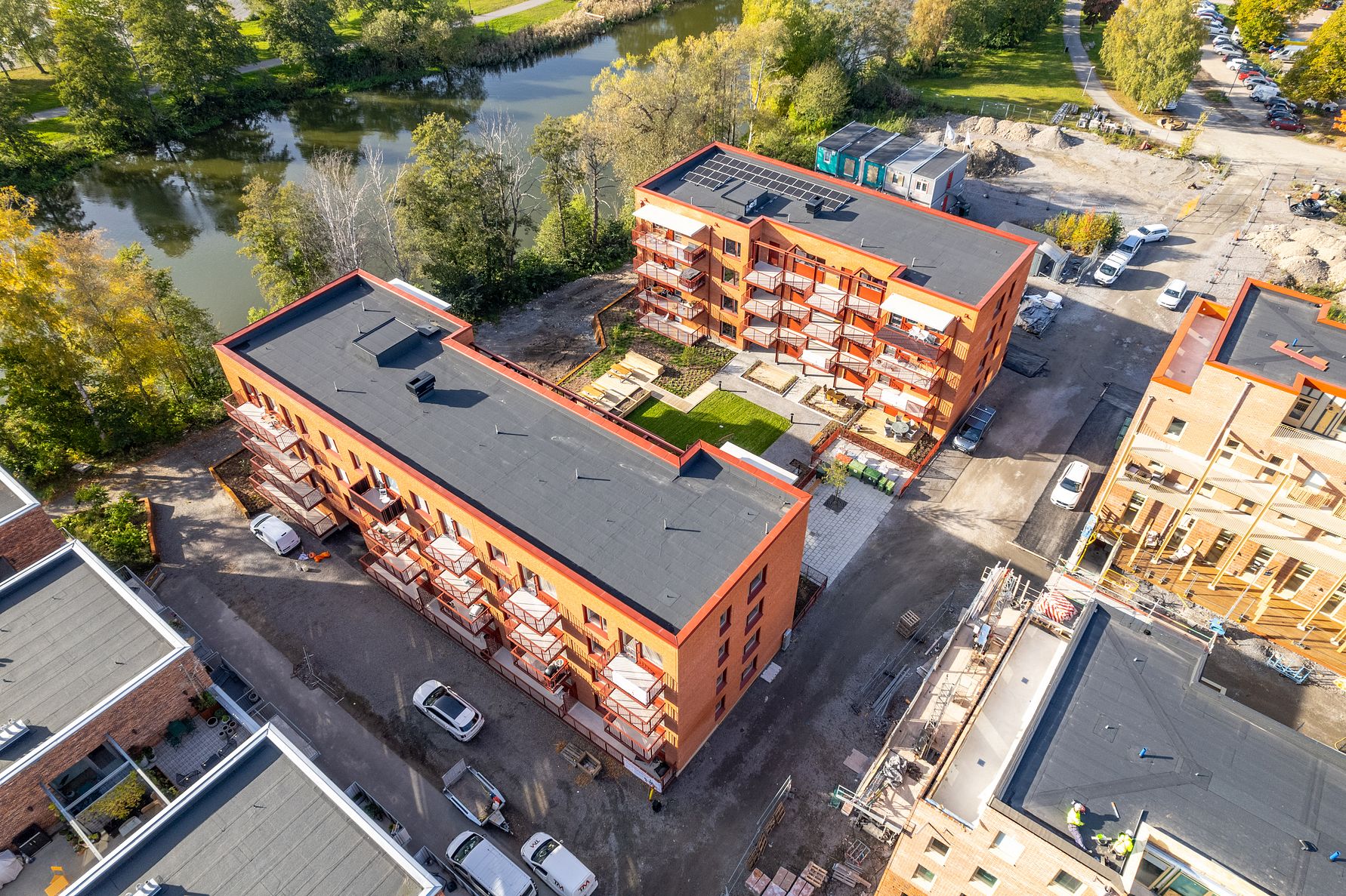 Flerbostadshus i tegel med innergård, omgivna av grönska och en vattenkanal