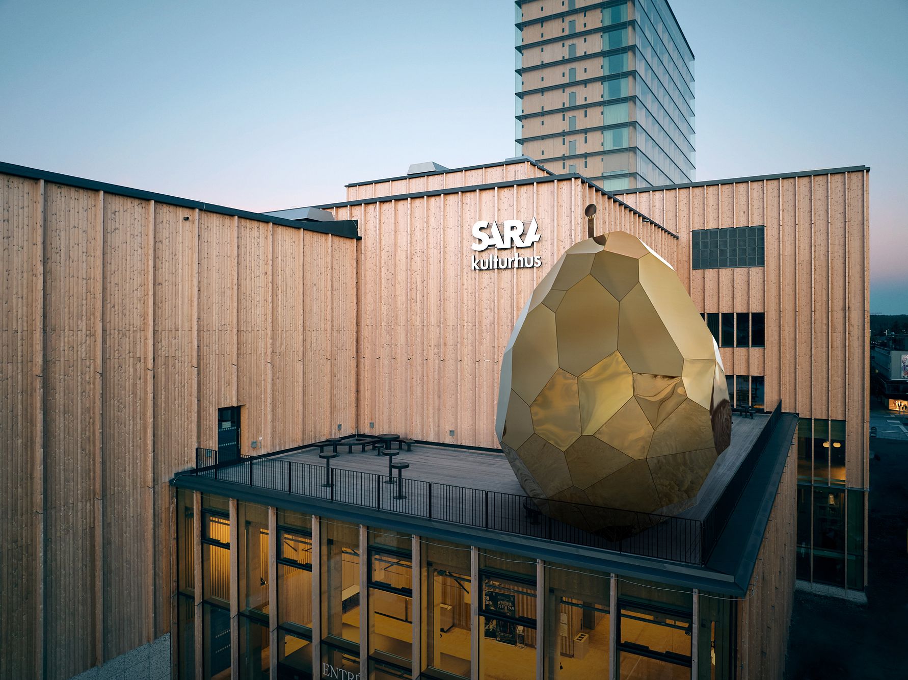 Träfasad av Sara Kulturhus i Skellefteå med en stor, guldfärgad ellipsoid på taket, omgiven av moderna byggnader