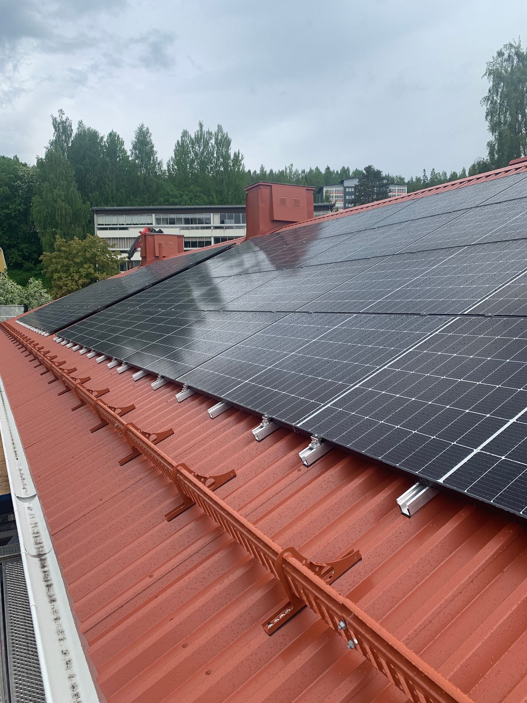 Solpaneler på ett rött tak under en molnig himmel, med träd och byggnader i bakgrunden