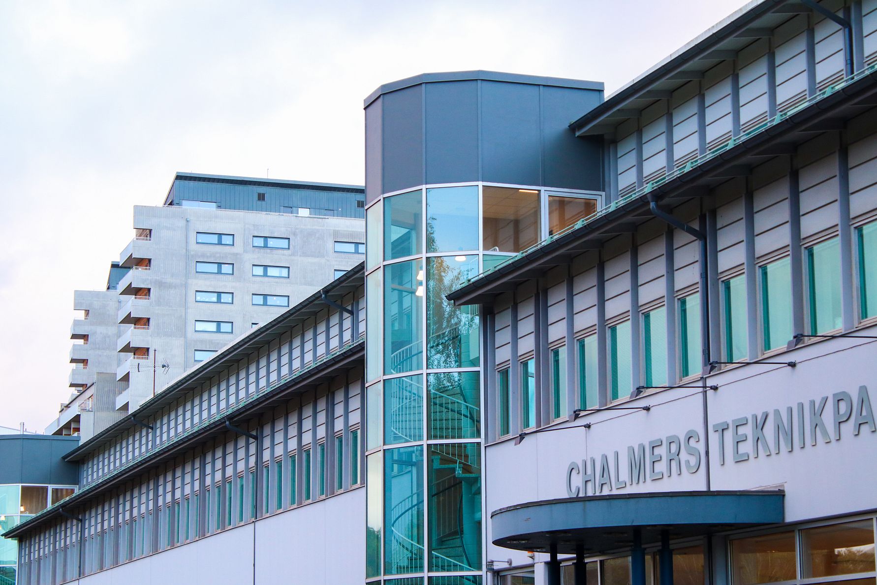 Byggnad med texten "Chalmers Teknologipark" på fasaden, med moderna glas- och betongdetaljer och ett flerfamiljshus i bakgrunden