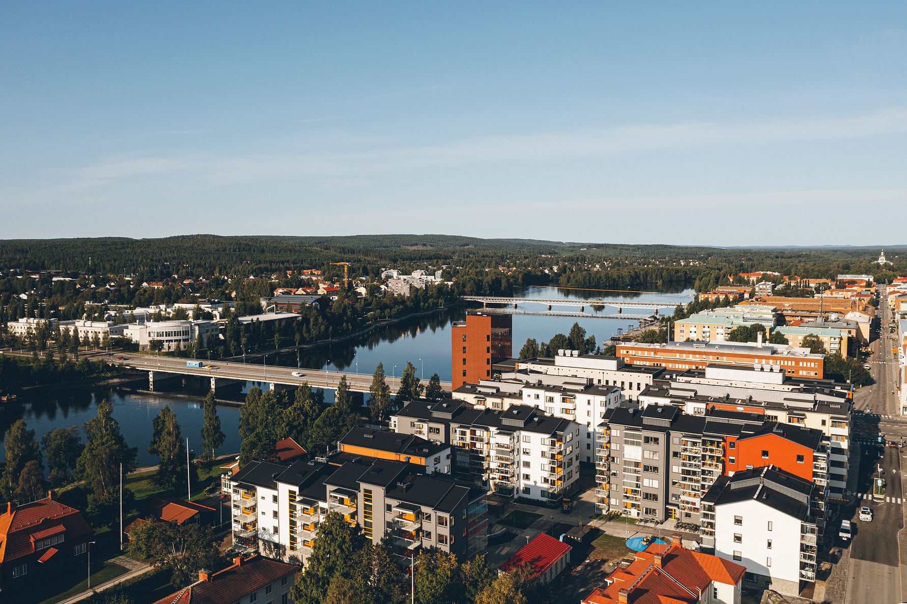 Vy över en stad med en flod som sträcker sig genom landskapet, omgiven av moderna byggnader och grönska under en klarblå himmel
