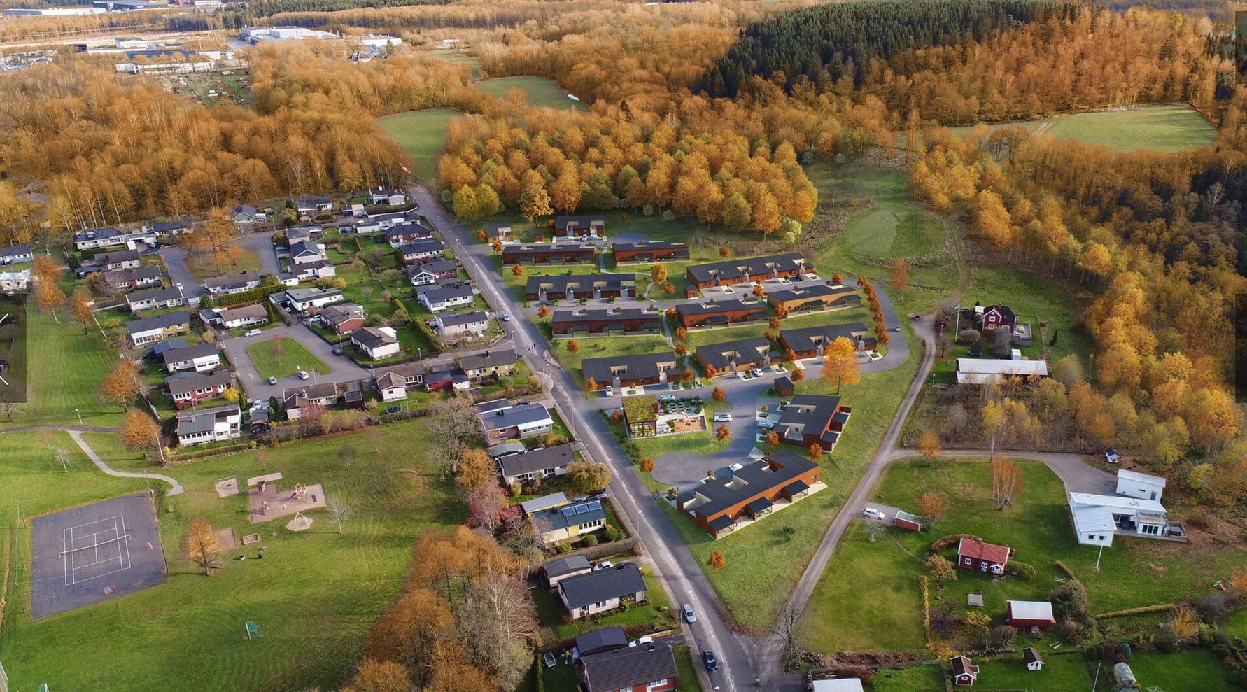 Flygvy över ett bostadsområde med hus, trädgårdar och omgivande skog i höstfärger. Grönområden, lekplatser och en väg synliga